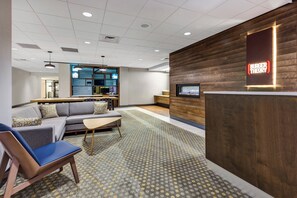 A modern reception area with a wooden reception desk, a seating area with a sofa and chairs, and a display wall with information.