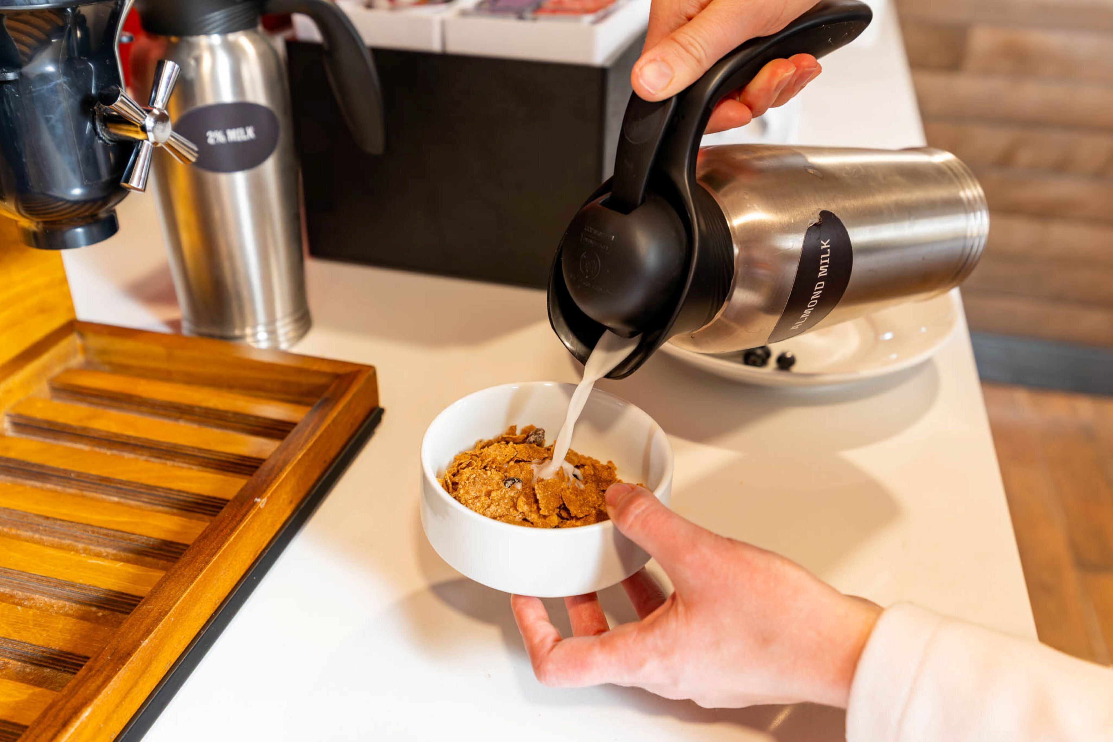 A person pouring milk into a bowl of cereal.