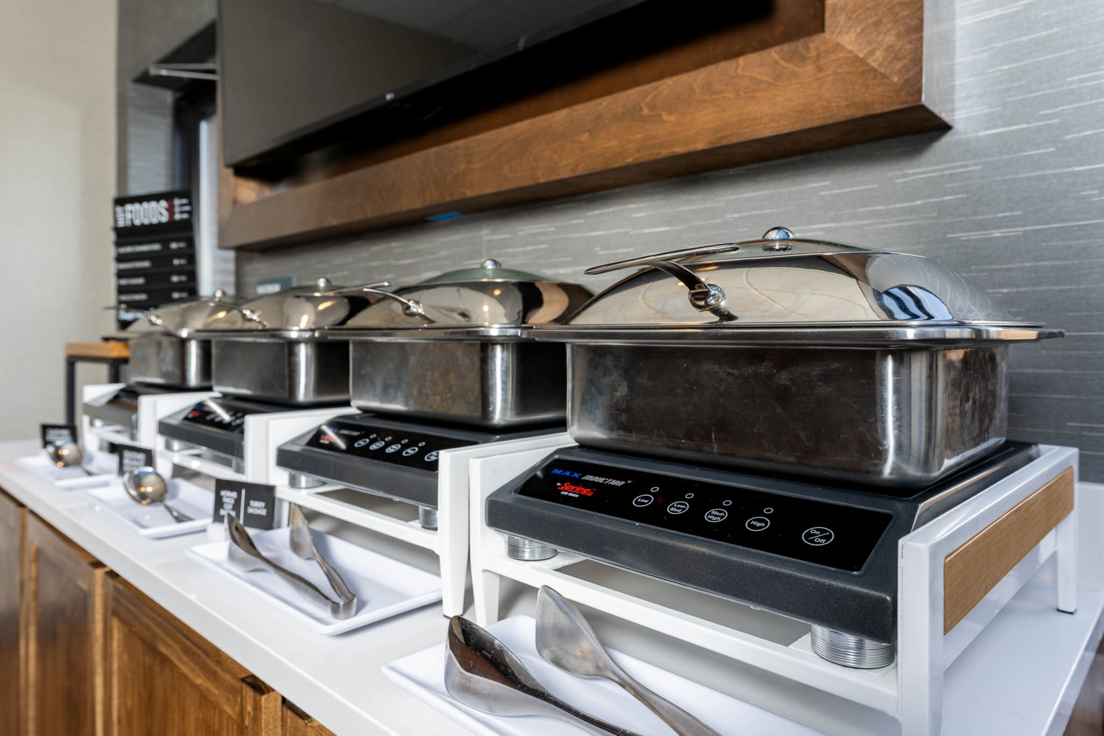 A buffet setup with multiple stainless steel chafing dishes on electric chafing stations, arranged on a white counter.