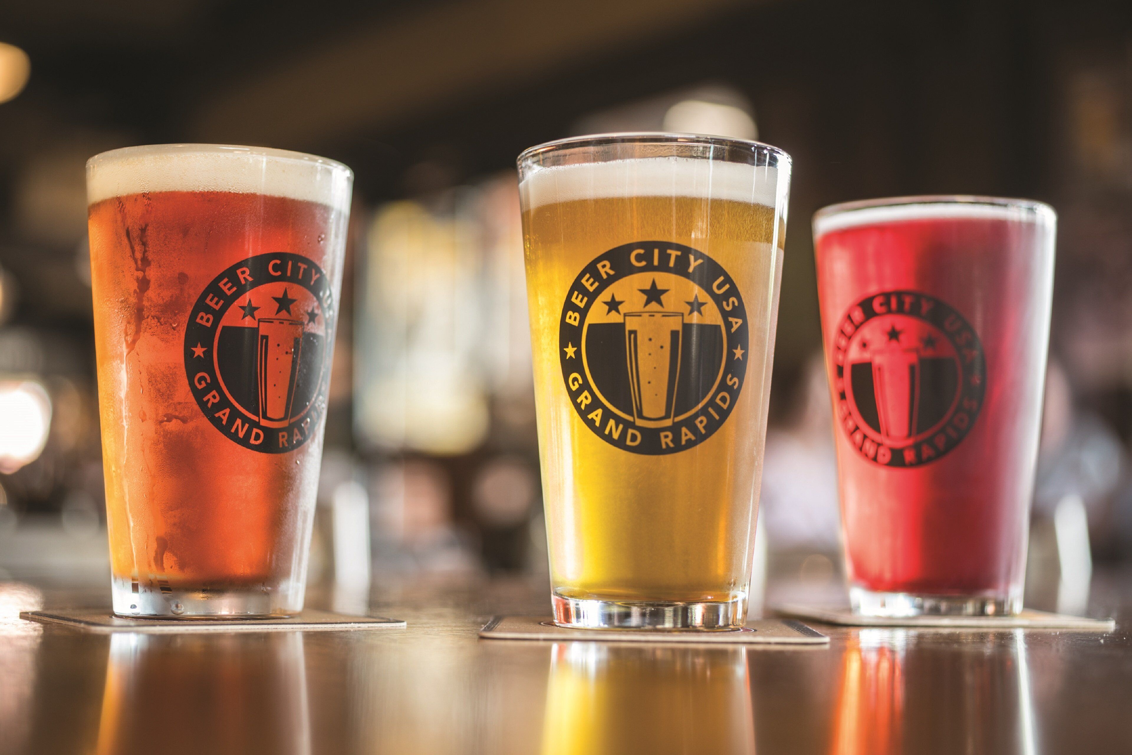 Three glasses of beer with different colors and logos, placed on a reflective surface.