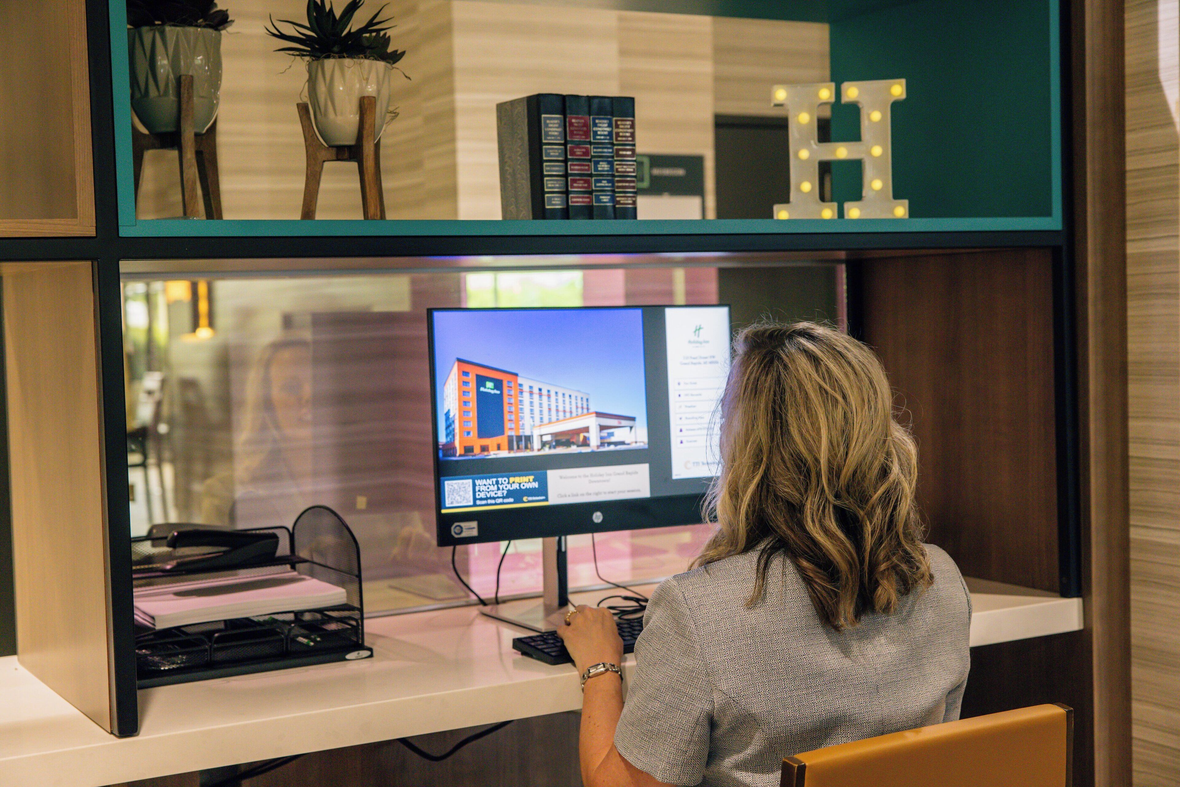 A hotel reception desk with a computer monitor displaying a building image, a keyboard, and a chair.