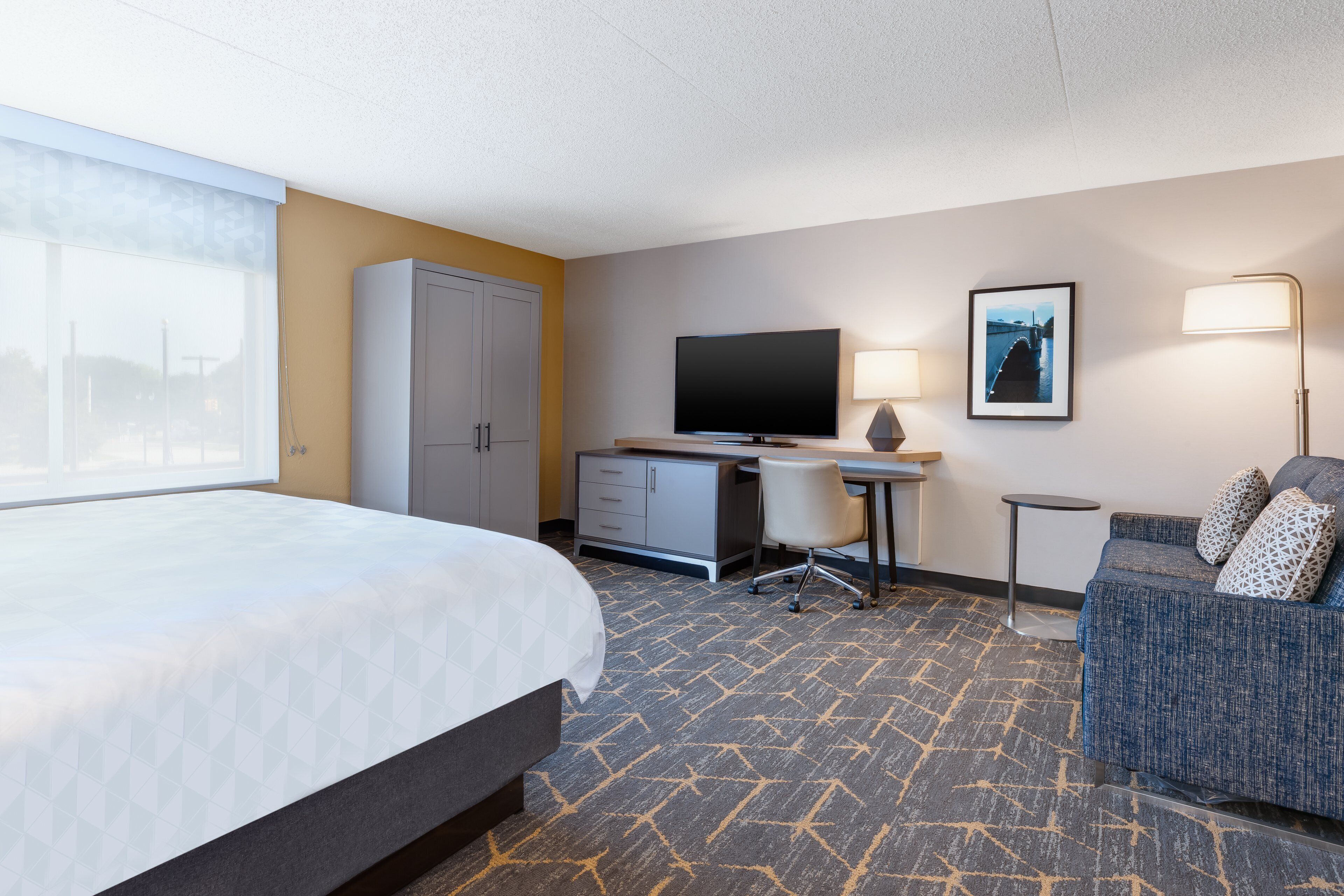 A hotel room with a bed, desk, TV, and a sofa.