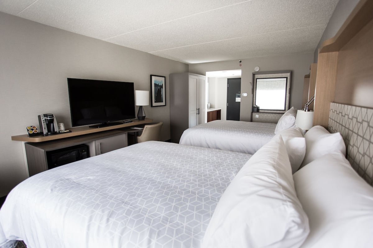 A hotel room with two beds, a TV, a desk with a computer, and a bathroom visible through an open door.