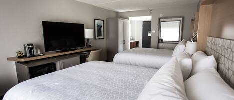 Quarto de hotel com duas camas, televisão, secretária com computador e casa de banho visível por uma porta aberta.