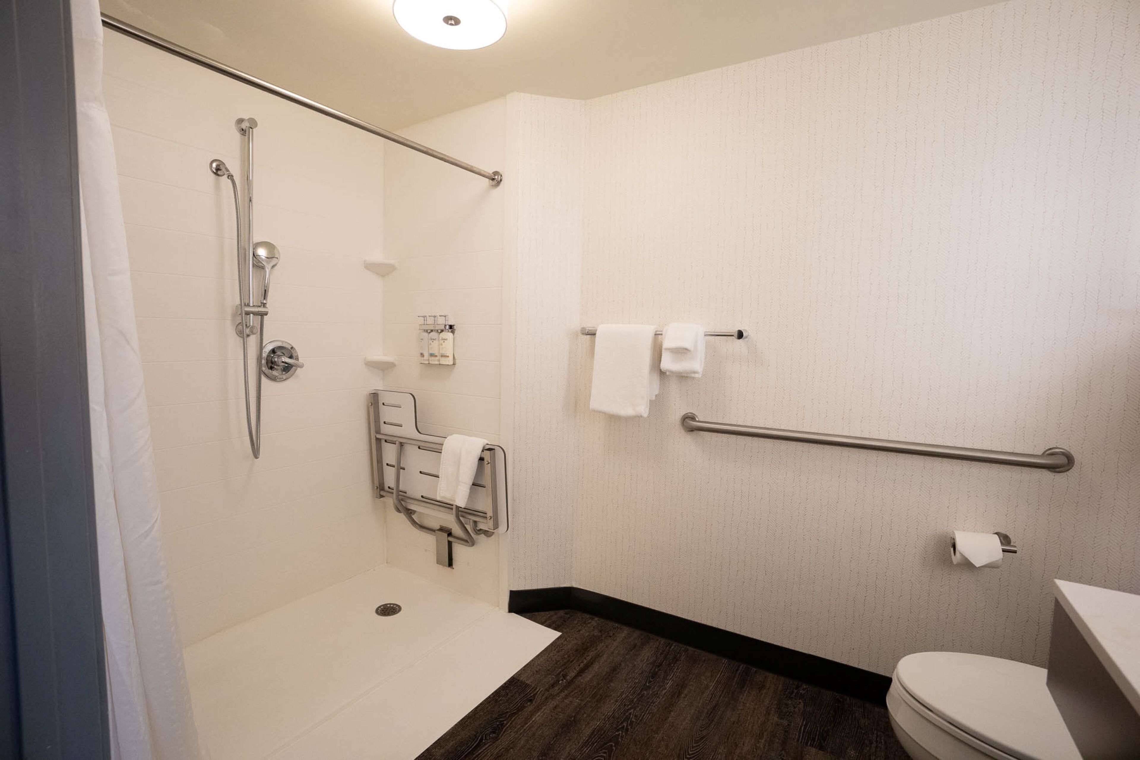 A bathroom with a shower, toilet, and grab bars.
