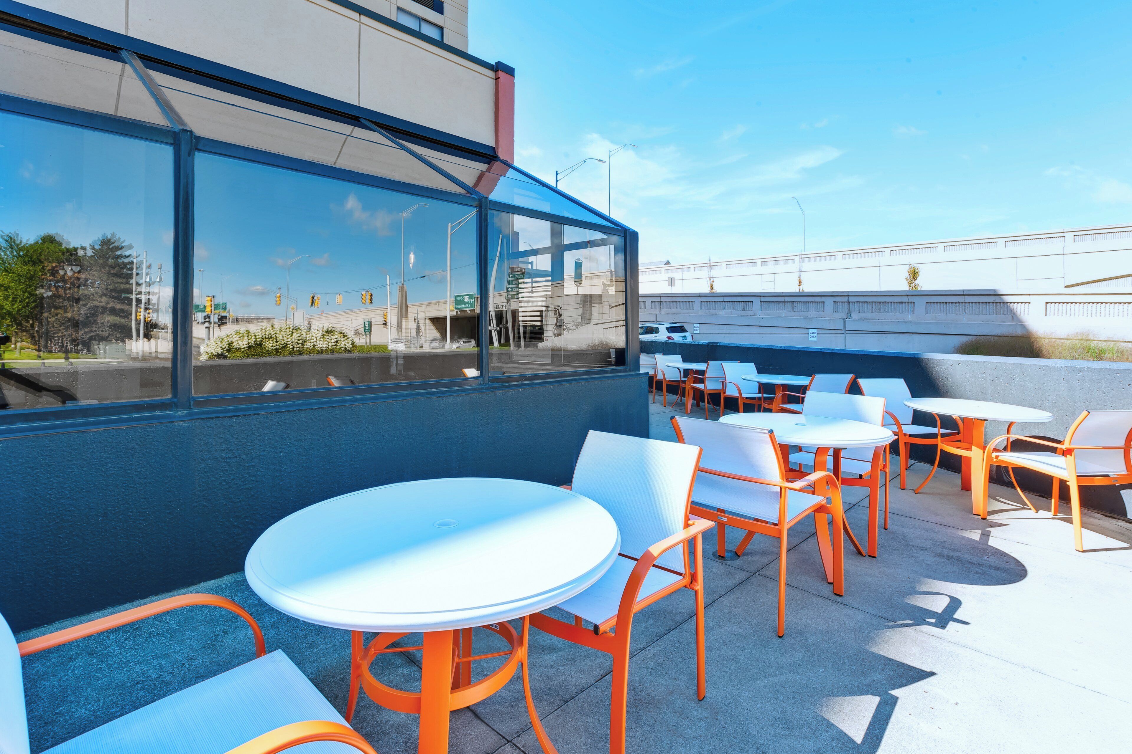An outdoor seating area with round tables and chairs, a view of the street, and a building with large windows.