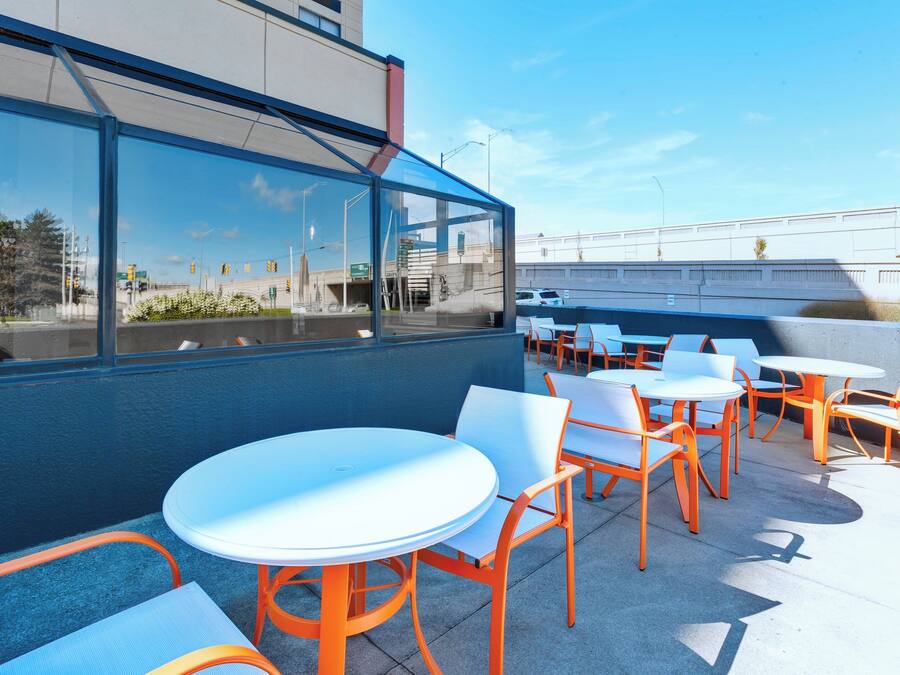An outdoor seating area with round tables and chairs, a view of the street, and a building with large windows.