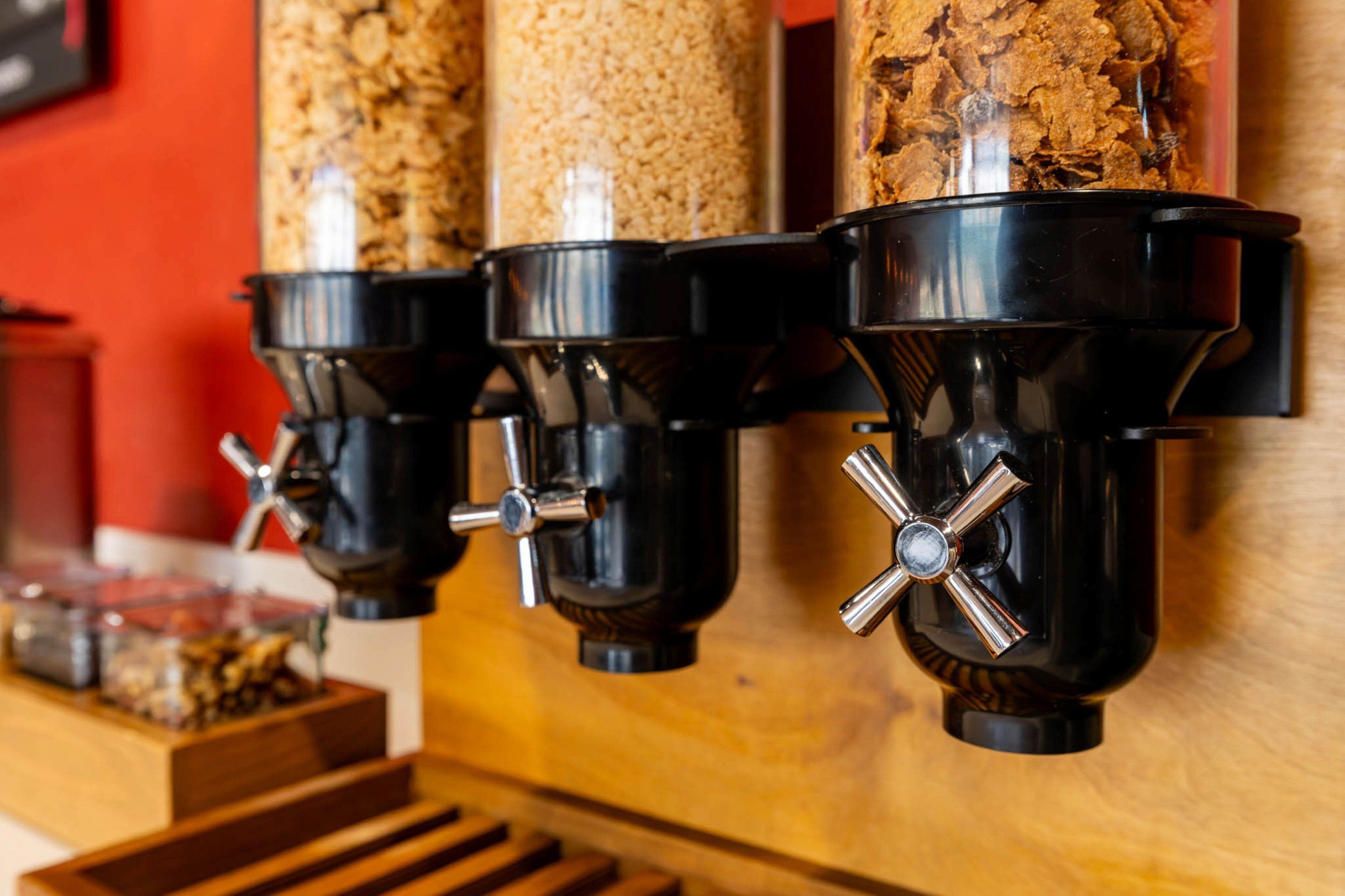 A coffee dispenser with multiple outlets, a wooden counter, and a container of granola.