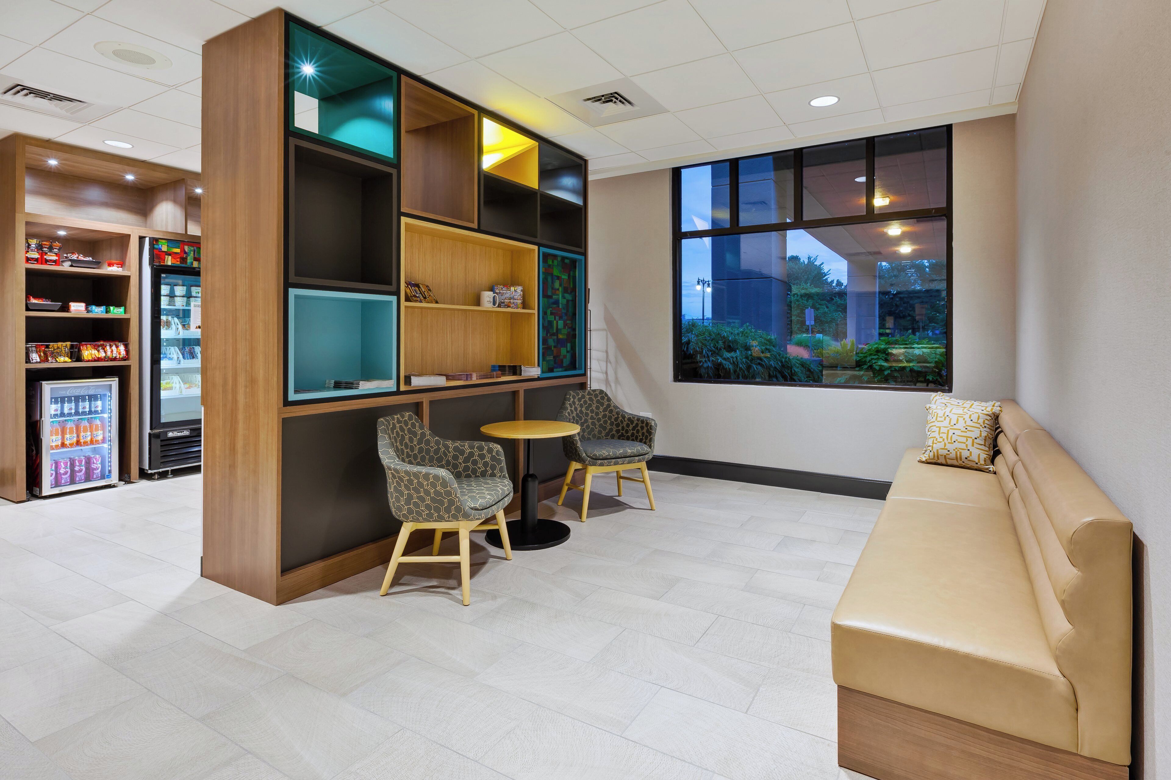 A modern lounge area with seating, a vending machine, and a large window.