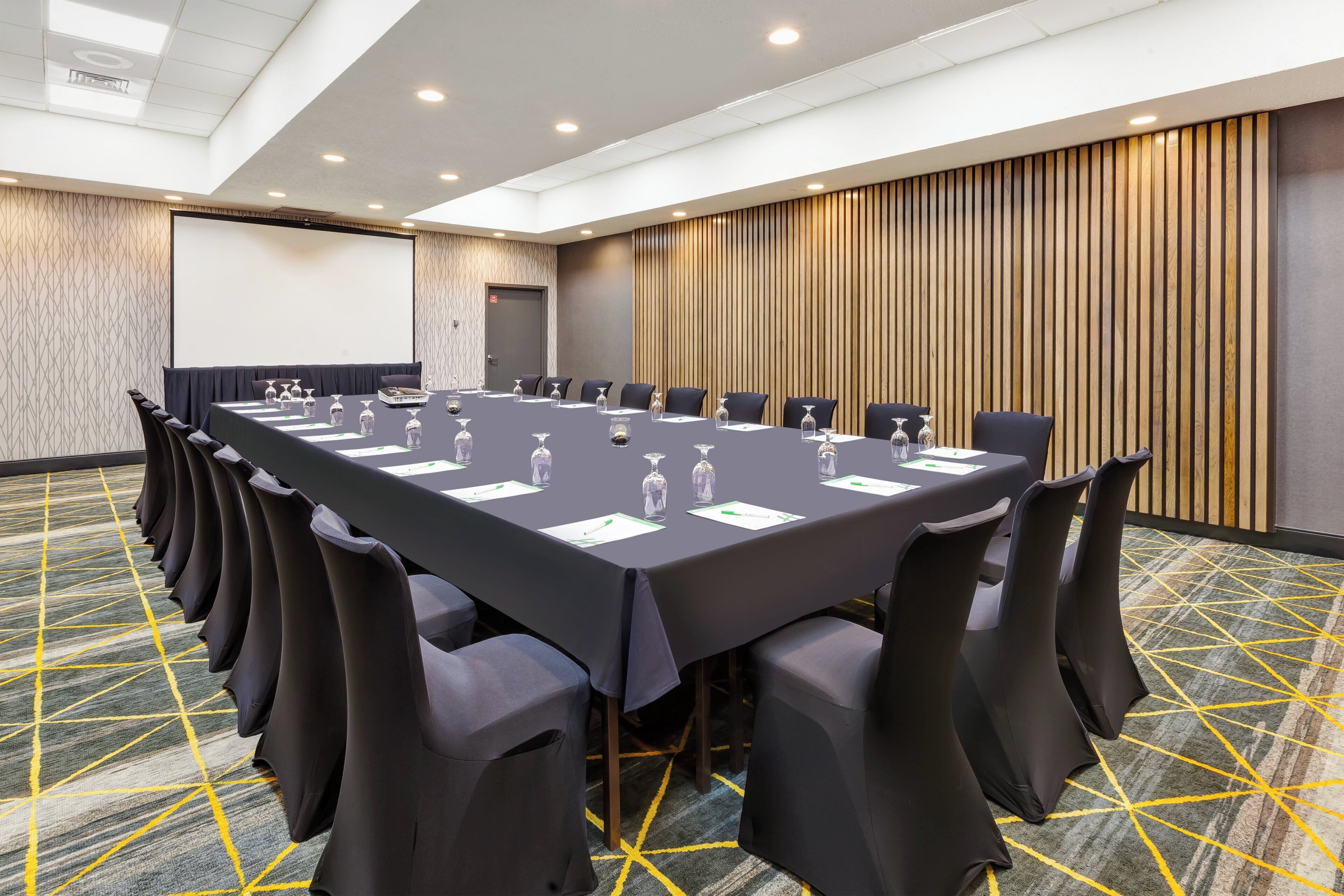 Una sala de conferencias con una larga mesa, sillas y una pantalla de proyector.