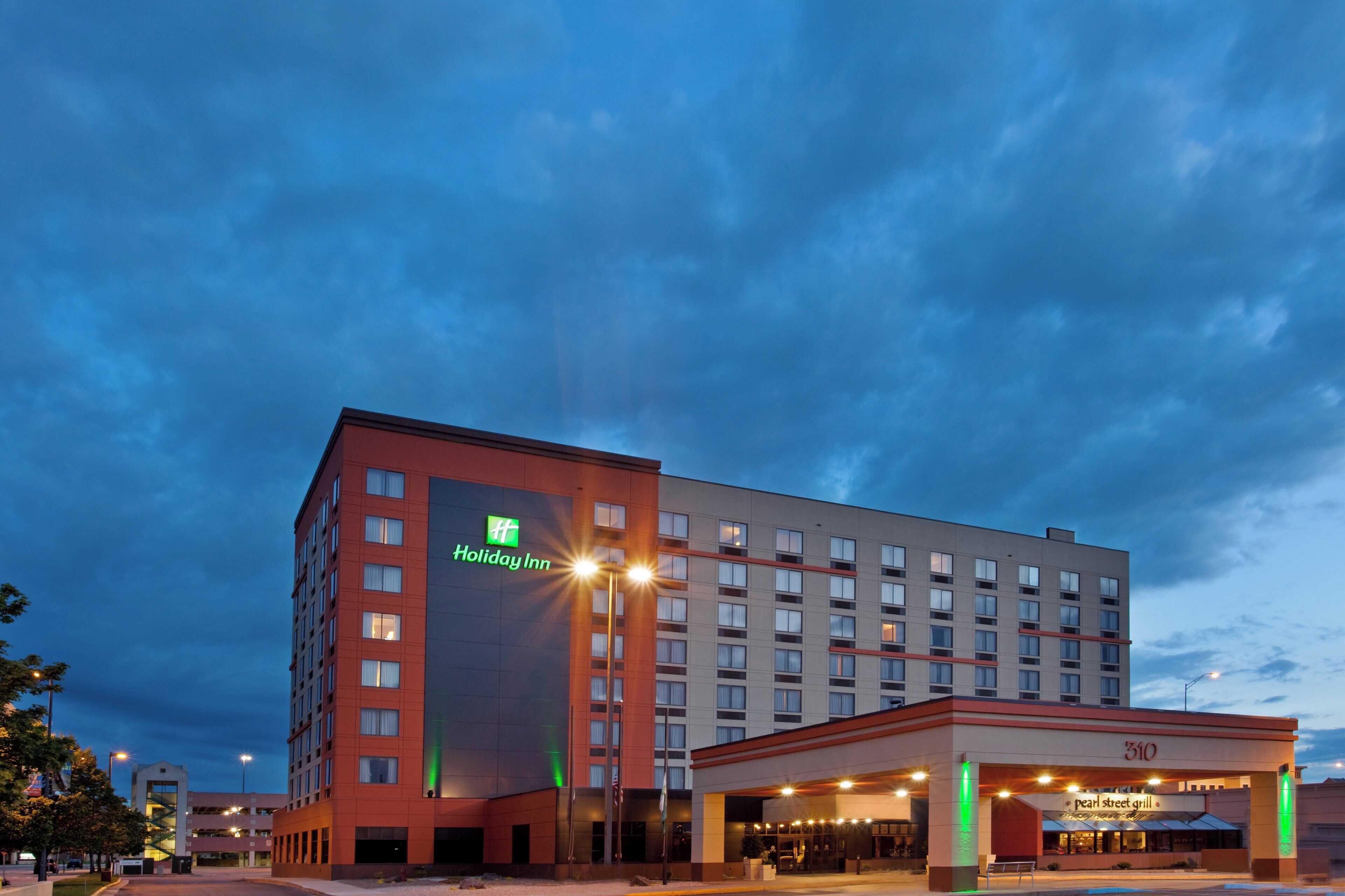 Un hotel Holiday Inn con diseño moderno, que destaca su logo verde, varios pisos y una zona de entrada bien iluminada.