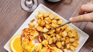 Un plato de comida con papas ralladas, una rodaja de naranja y una loncha de jamón.