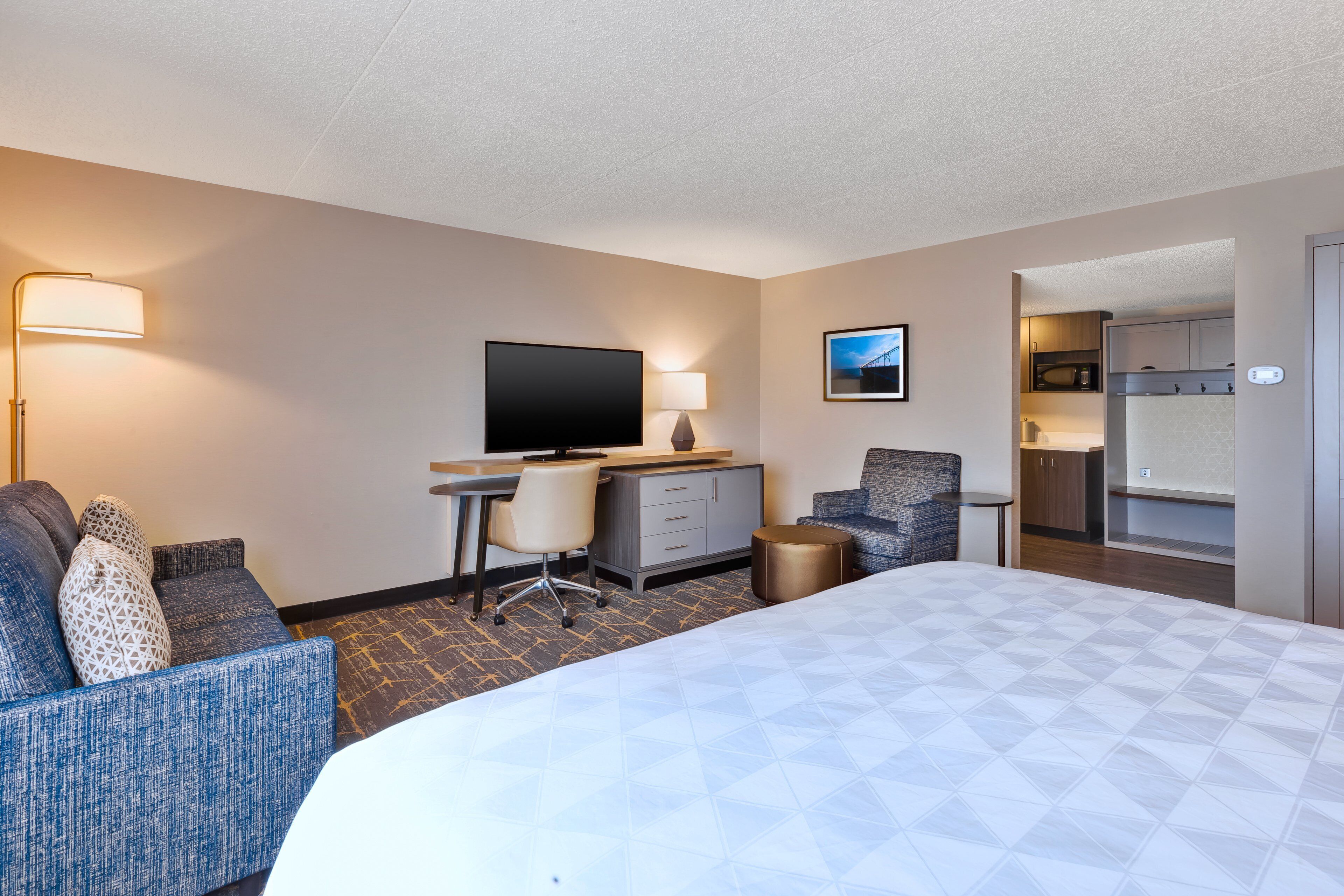 Une chambre d’hôtel comprenant un lit, un bureau avec une chaise, une télévision et une kitchenette.