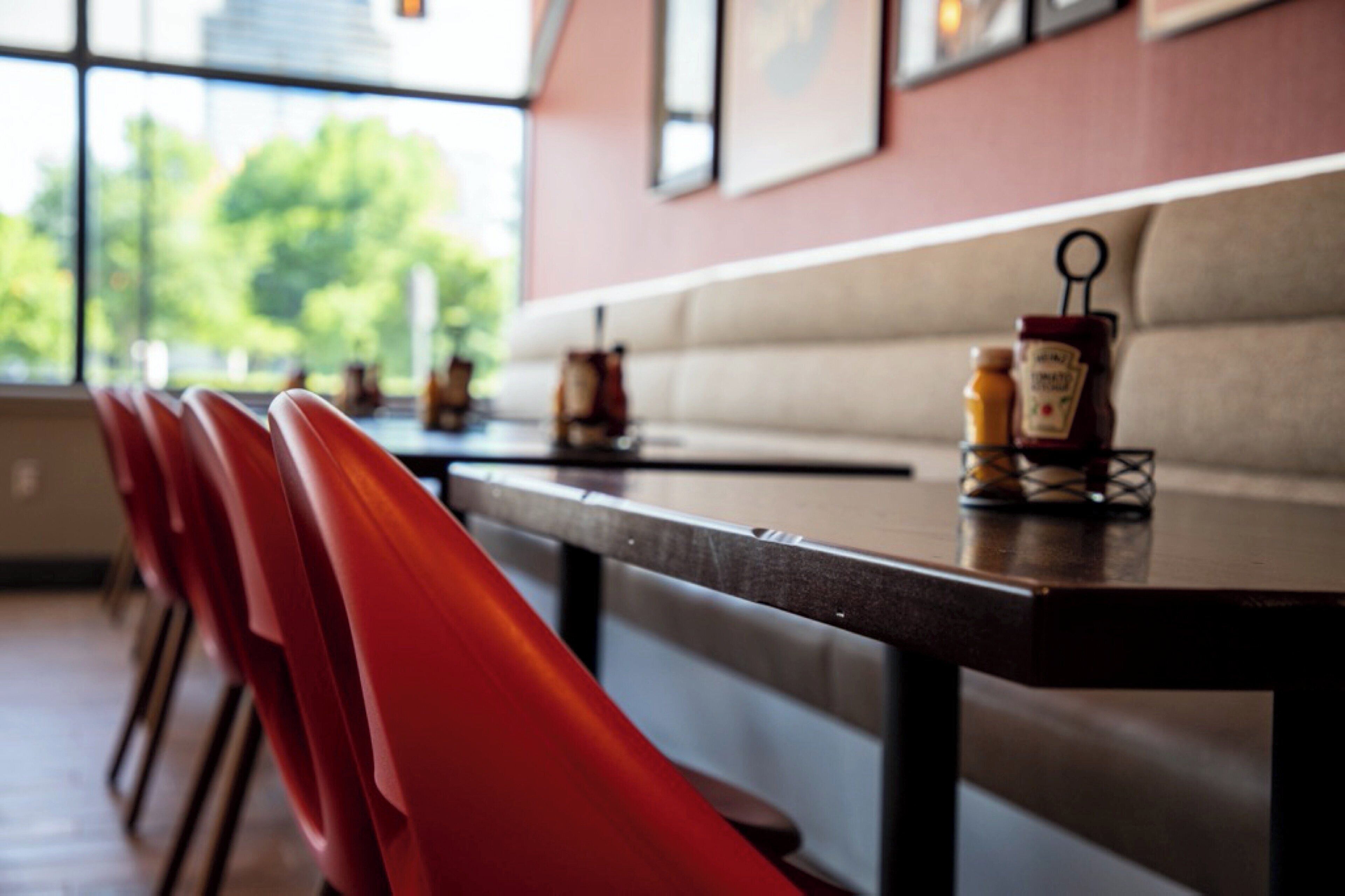 A restaurant interior with a long table, red chairs, and a bench.