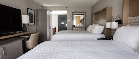 A hotel room with two beds, a desk with a TV, a chair, and a mirror.