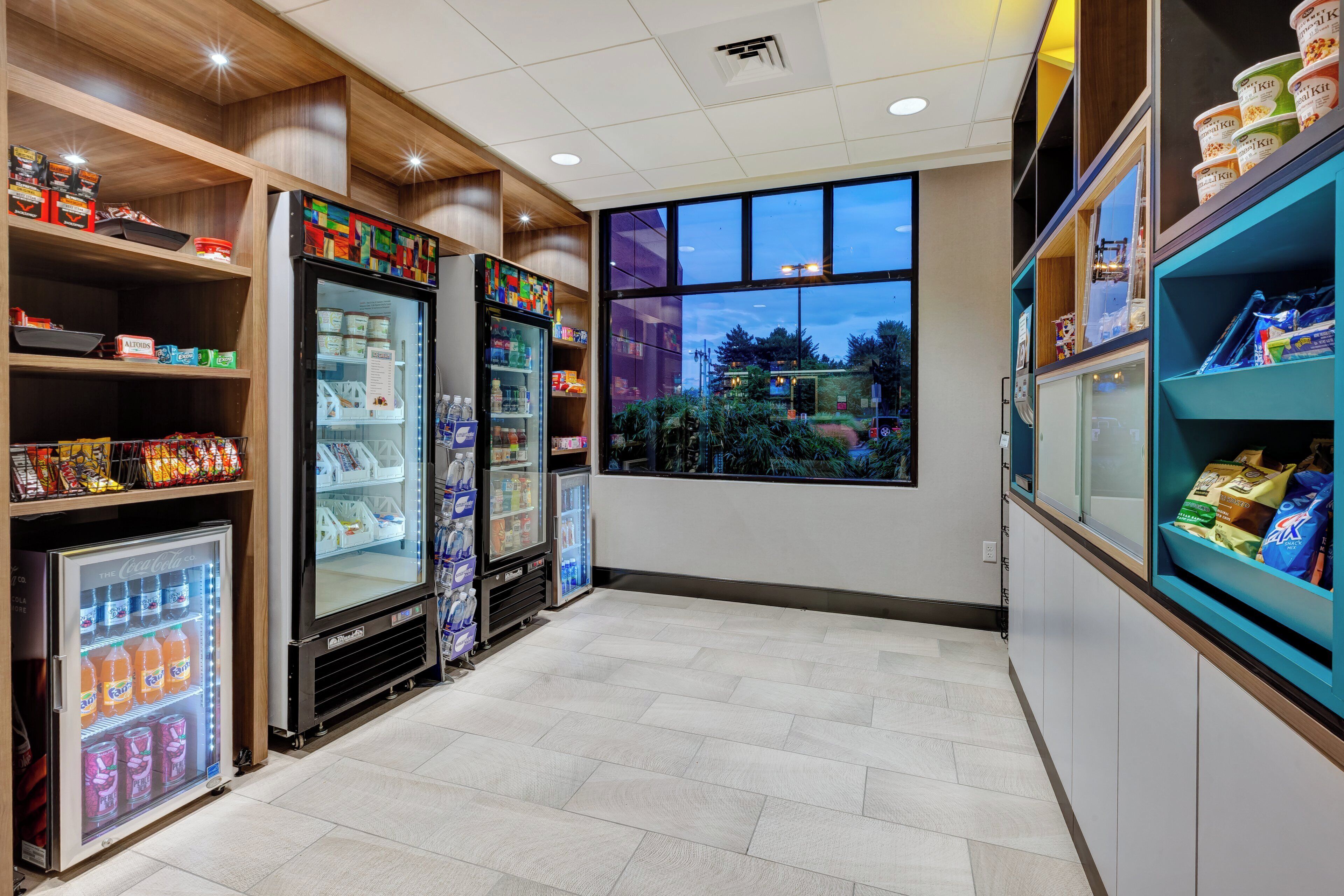 Una barra de aperitivos con vitrinas refrigeradas, estantes llenos de productos y un amplio ventanal con vistas al exterior.