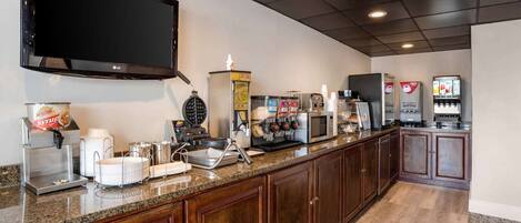 A kitchen with a flat-screen TV, coffee machines, a waffle maker, and a refrigerator.