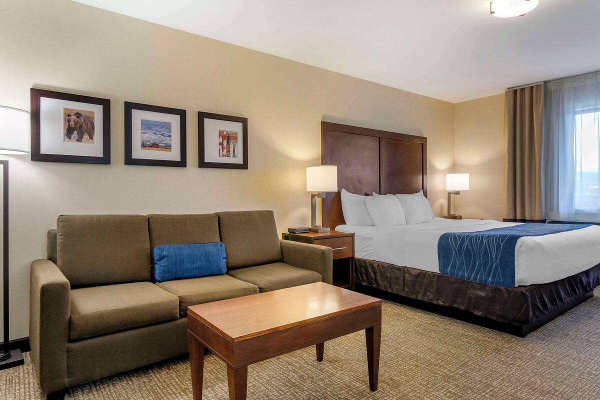 A hotel room with a bed, a sofa, a coffee table, and three framed pictures on the wall.
