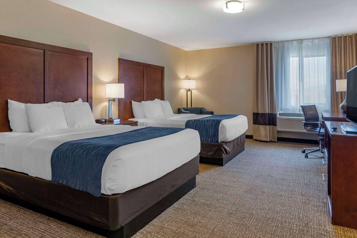 A hotel room with two beds, a desk, a chair, and a television.
