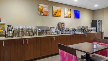 A breakfast bar with coffee machines, a bread machine, and a refrigerator. There are wall-mounted pictures of food items and a sign that says "RICE & SHINE".