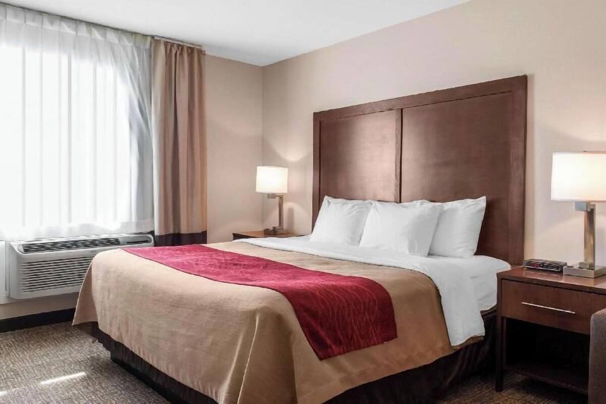 A hotel room with a bed, two bedside lamps, a desk with a lamp, and a window with curtains.