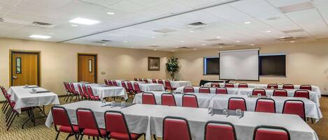 A conference room with multiple tables and chairs, a projector screen, and a whiteboard.