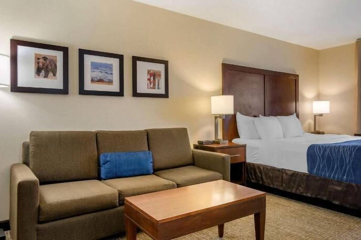 A hotel room with a bed, a sofa, a coffee table, and three framed pictures on the wall.