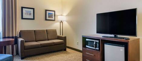 A hotel room with a sofa, a small table, a TV, a mini-fridge, and a lamp.