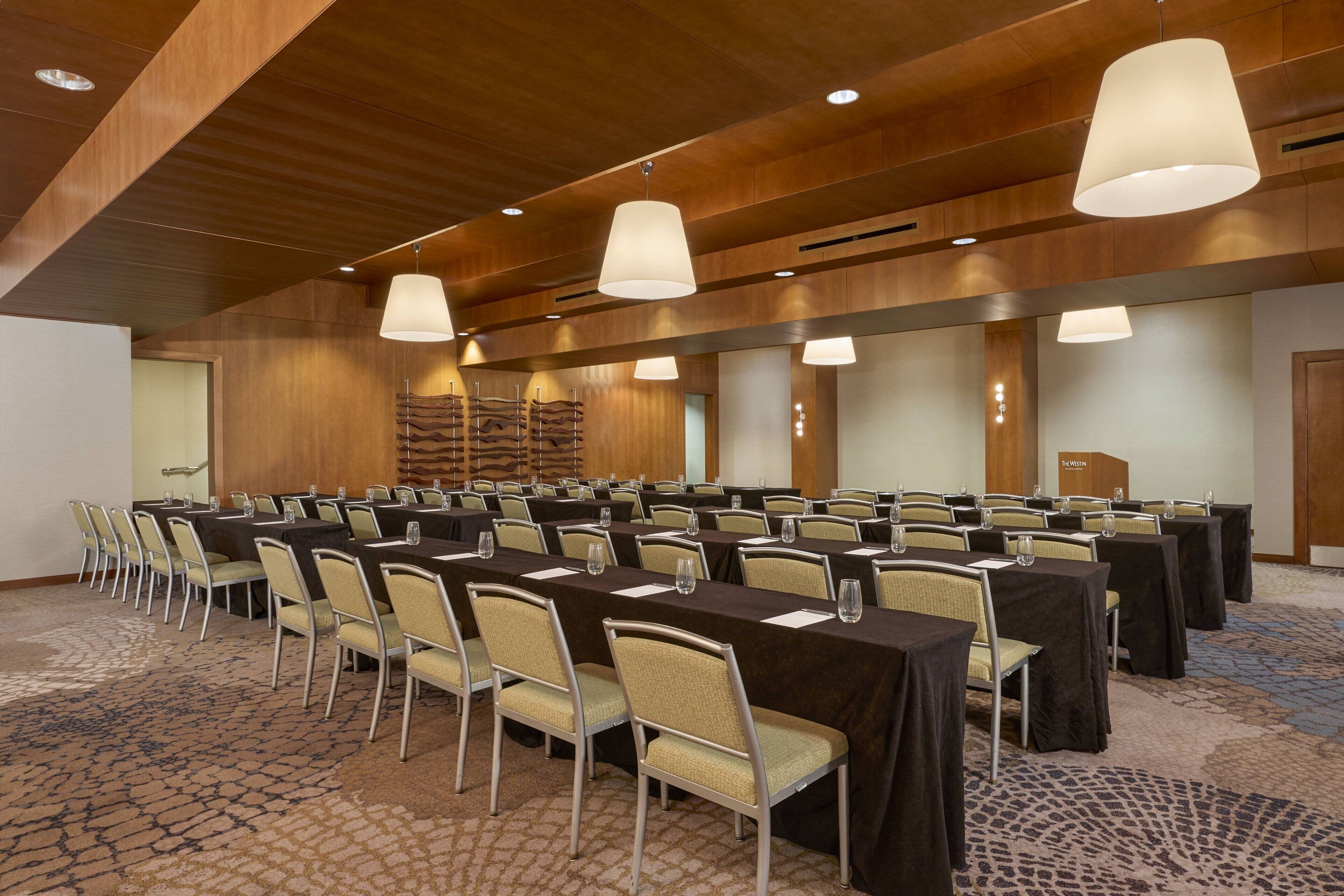 A conference room with rows of tables and chairs, wooden panel walls, and pendant lighting.