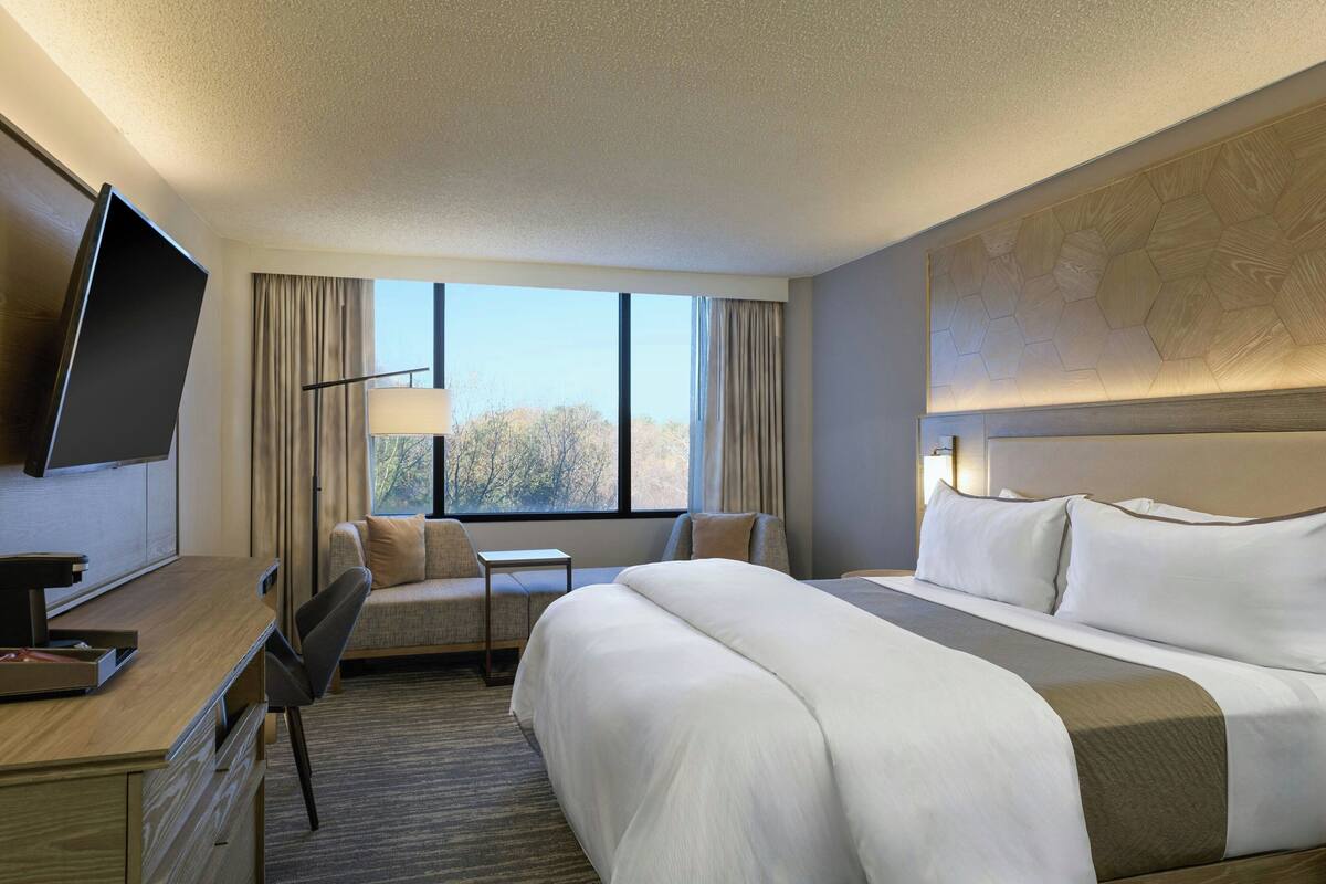 A hotel room with a large bed, a desk with a chair, a television, and a window with curtains.