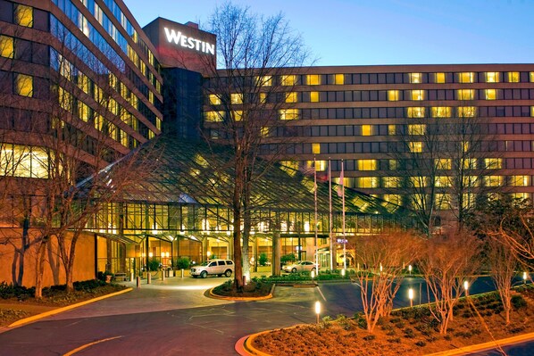 Un hotel Westin con fachada de vidrio moderna, entrada cubierta y camino de acceso arbolado.