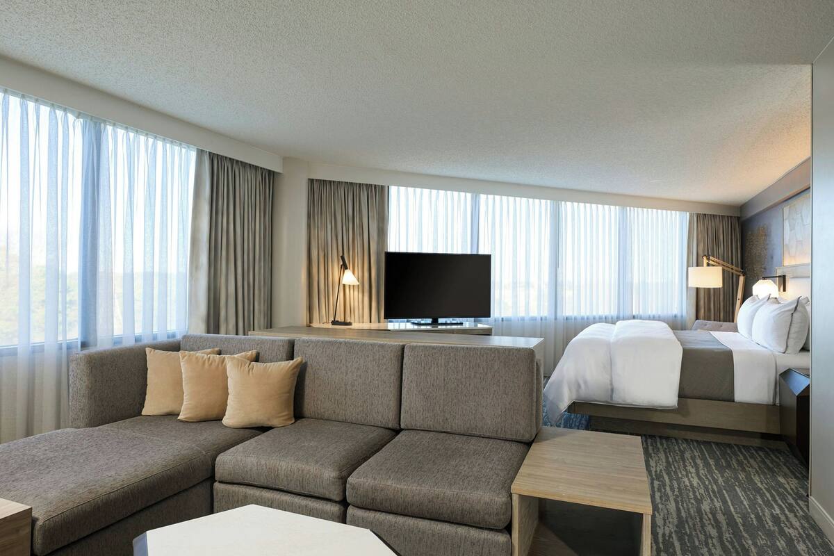 A modern hotel room with a sofa, a bed, a TV, and a desk.
