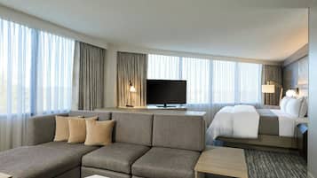 A modern hotel room with a sofa, a bed, a TV, and a desk.