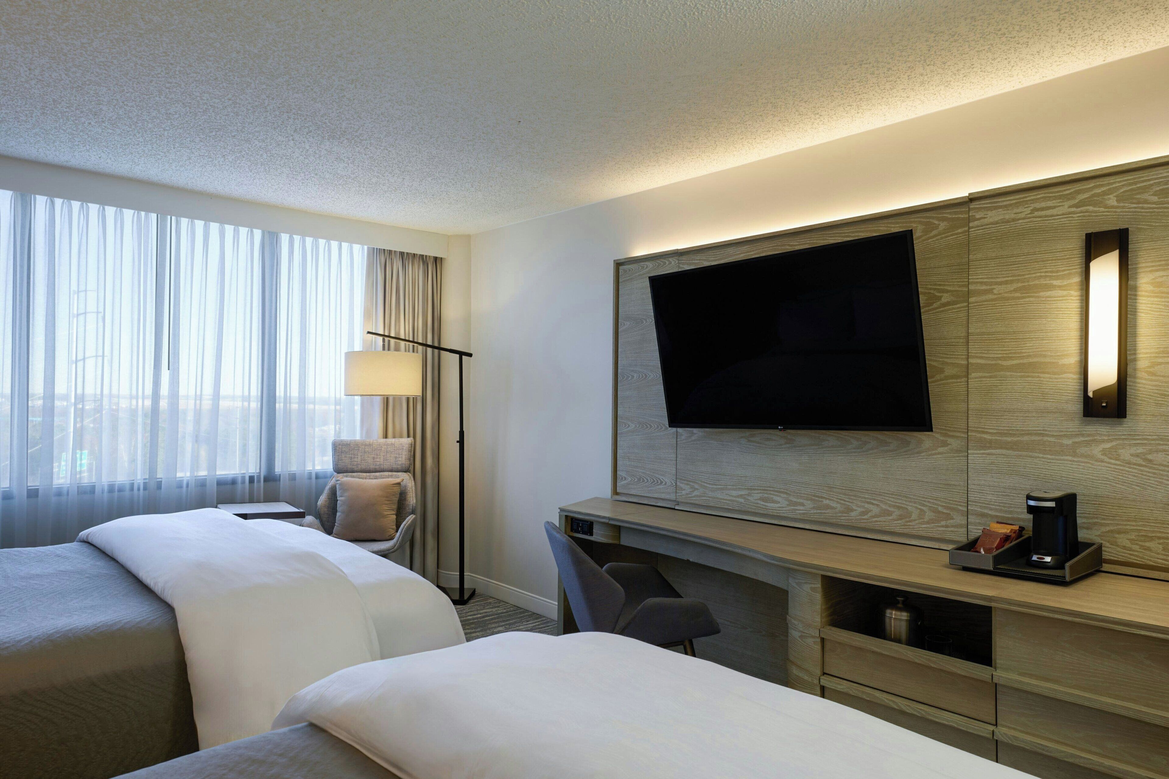 A hotel room with two beds, a desk, a TV, and a lamp.
