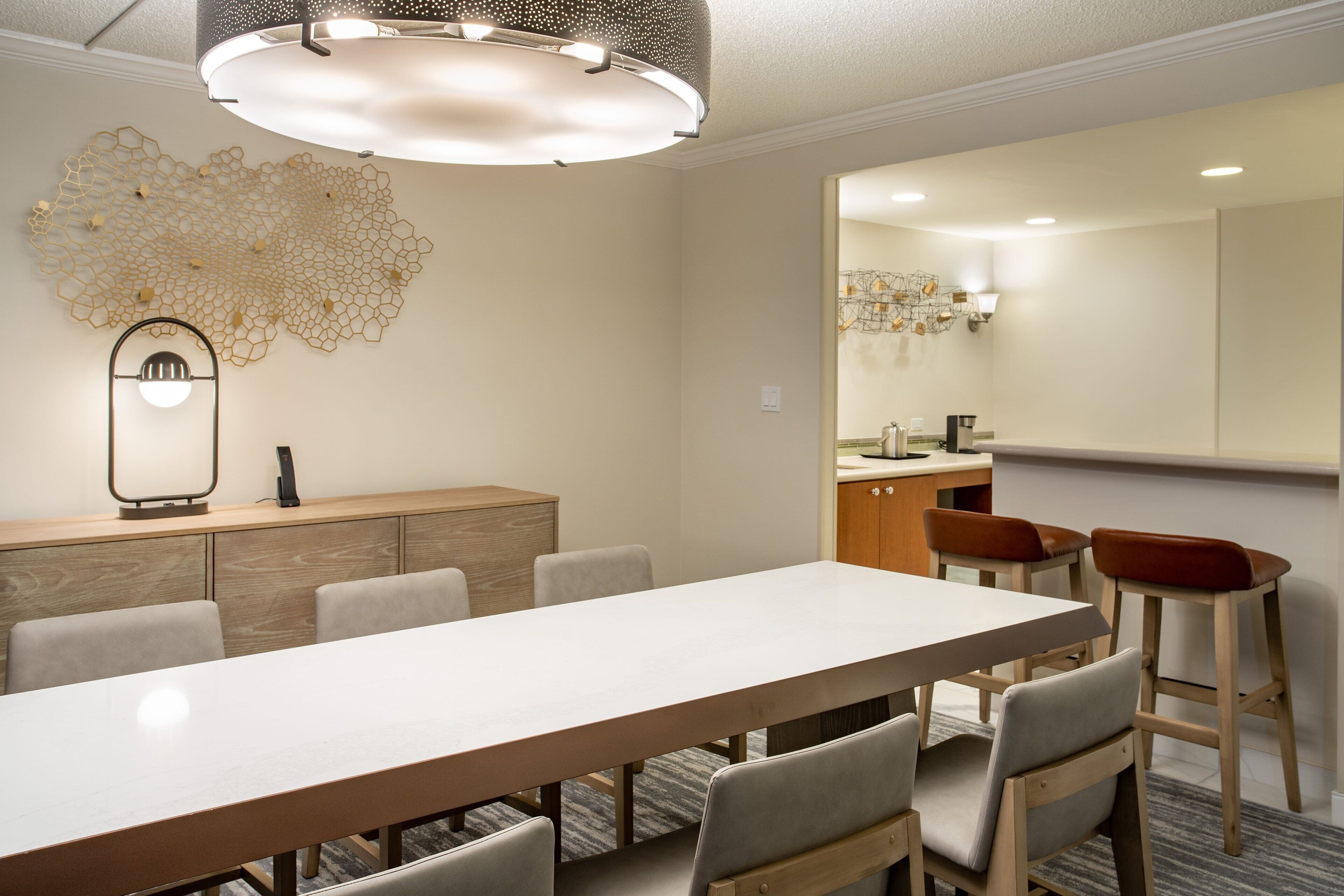 Un espace de salle à manger moderne, avec une longue table, plusieurs chaises, un élément décoratif mural et un grand miroir.