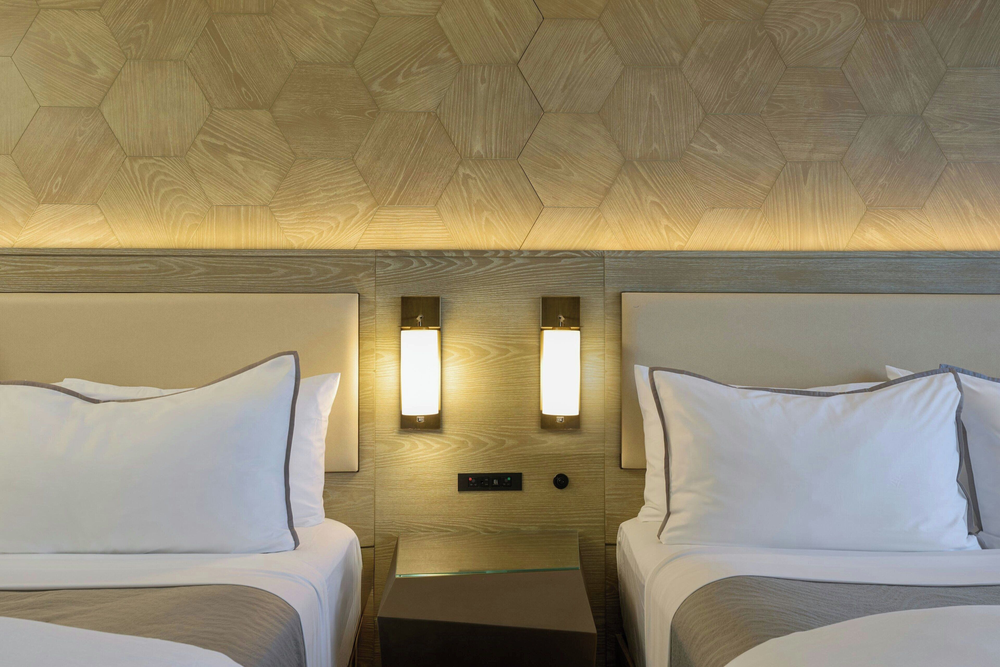 A hotel room with two beds, wooden ceiling, and wall-mounted lighting.