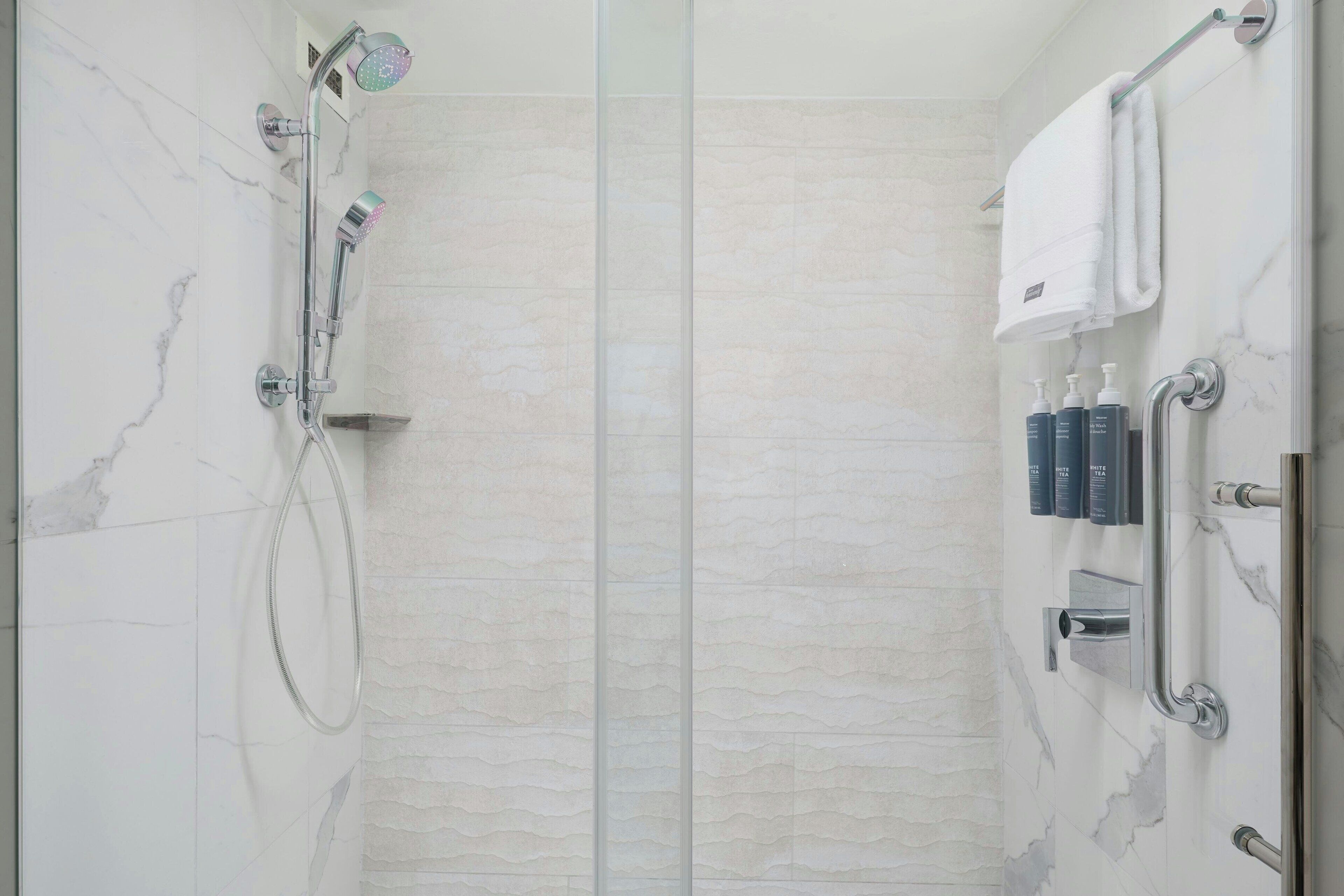 A modern shower with a handheld showerhead, a glass-enclosed shower area, and a towel rack with toiletries.