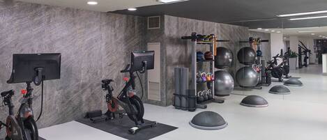 Academia moderna com bicicletas ergométricas, uma máquina de remo e diversos colchonetes de exercício.