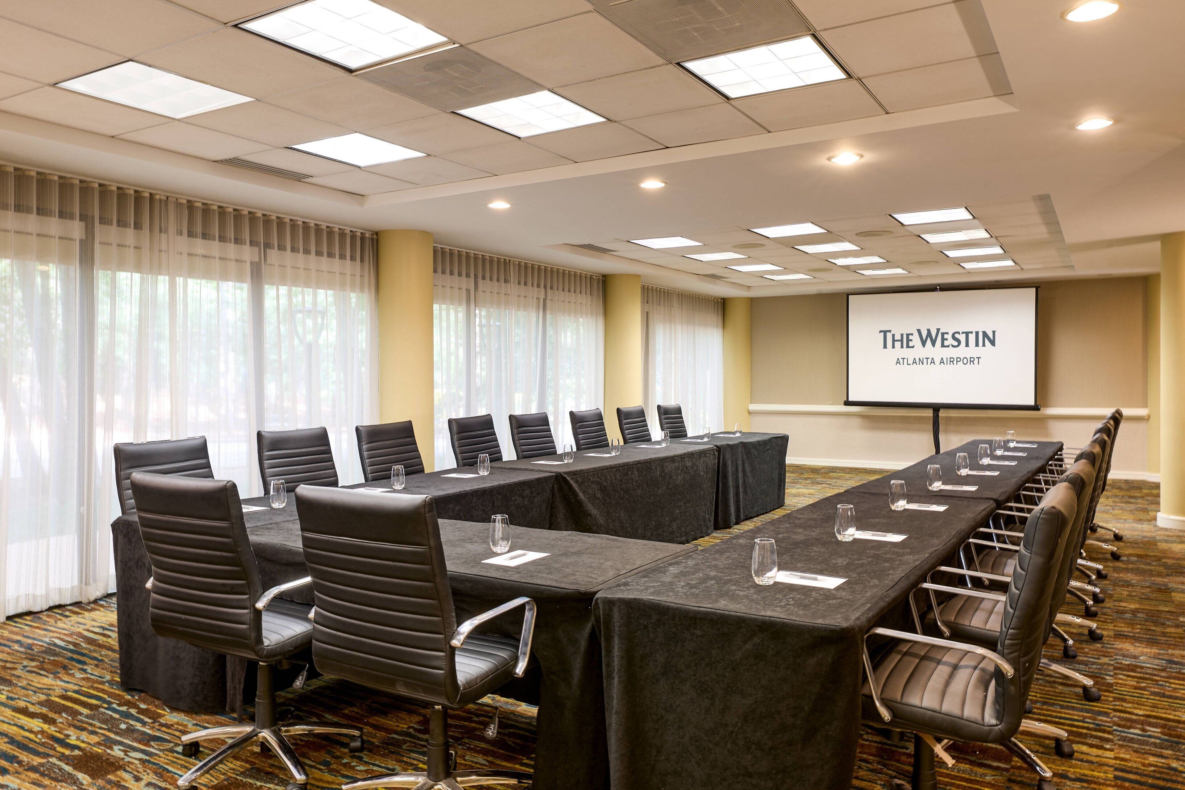 A conference room with a long table, chairs, a projector screen, and a carpeted floor.
