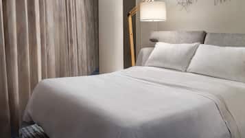 A neatly made bed with white linens, a floor lamp, and a wall art piece.