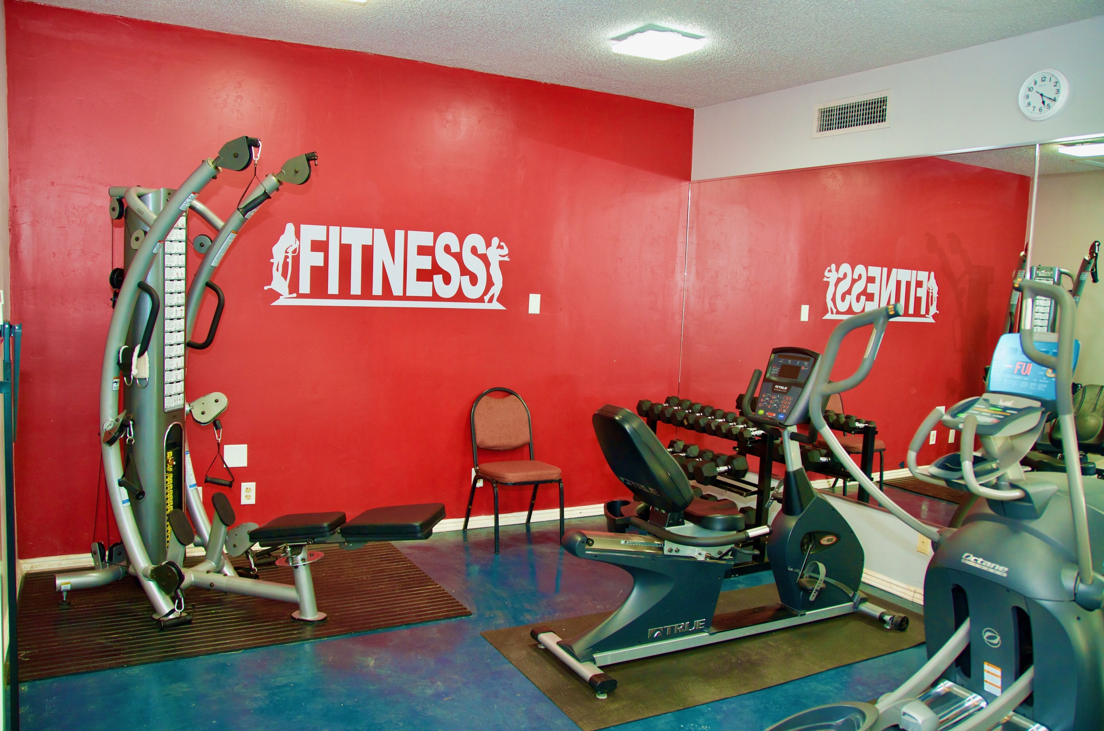 A gym with red walls, exercise equipment, and a chair.
