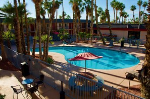 A swimming pool with a red umbrella, surrounded by palm trees and a fence. - Ramada by Wyndham Yuma (Yuma)