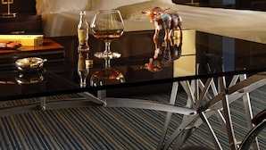 A hotel room with a bed, a glass coffee table, a bottle of Metaxa, a glass of whiskey, and a decorative horse figurine. - Crowne Plaza Athens City Centre by IHG (Athens)