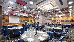 Une salle de conférence avec des tables rondes, des chaises bleues et un écran de projection.