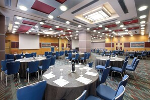 A conference room with round tables, blue chairs, and a projector screen. - Crowne Plaza Athens City Centre by IHG (Athens)