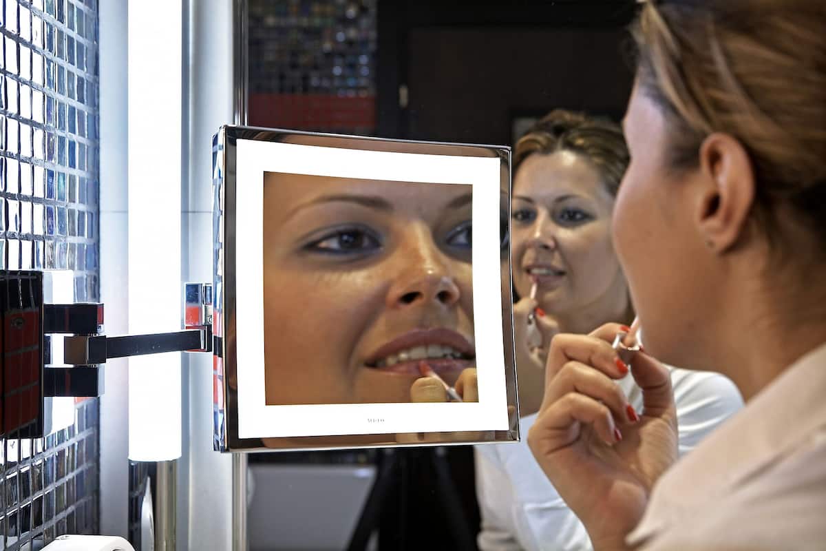 A person using a mirror with a digital display, possibly for makeup application.