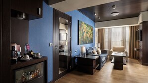 Une chambre d’hôtel moderne dotée d’un espace salon, d’une kitchenette et d’une grande fenêtre avec des rideaux.