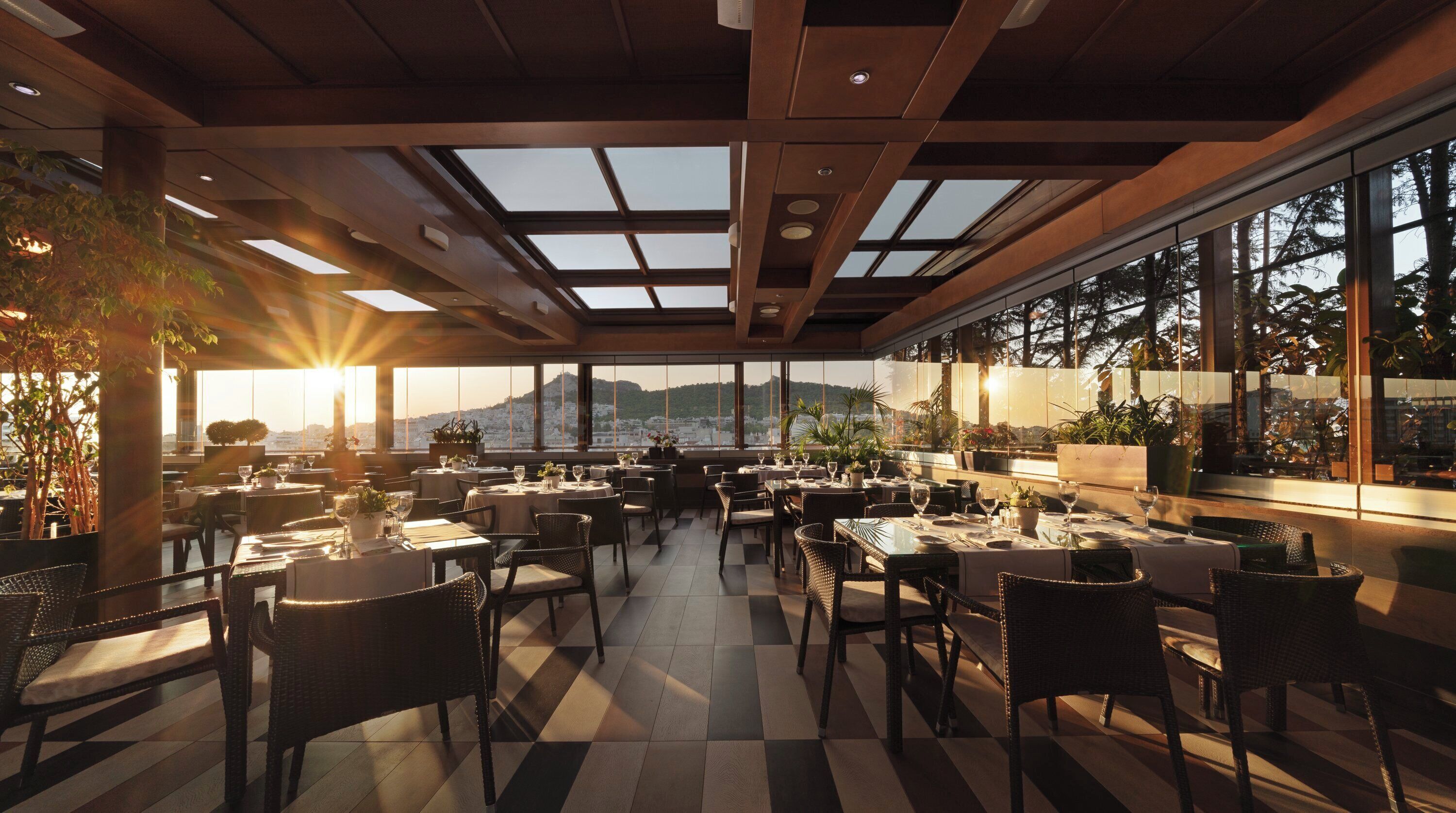 Un restaurante con piso a cuadros, mesas dispuestas para comer y grandes ventanales con vistas a la ciudad.