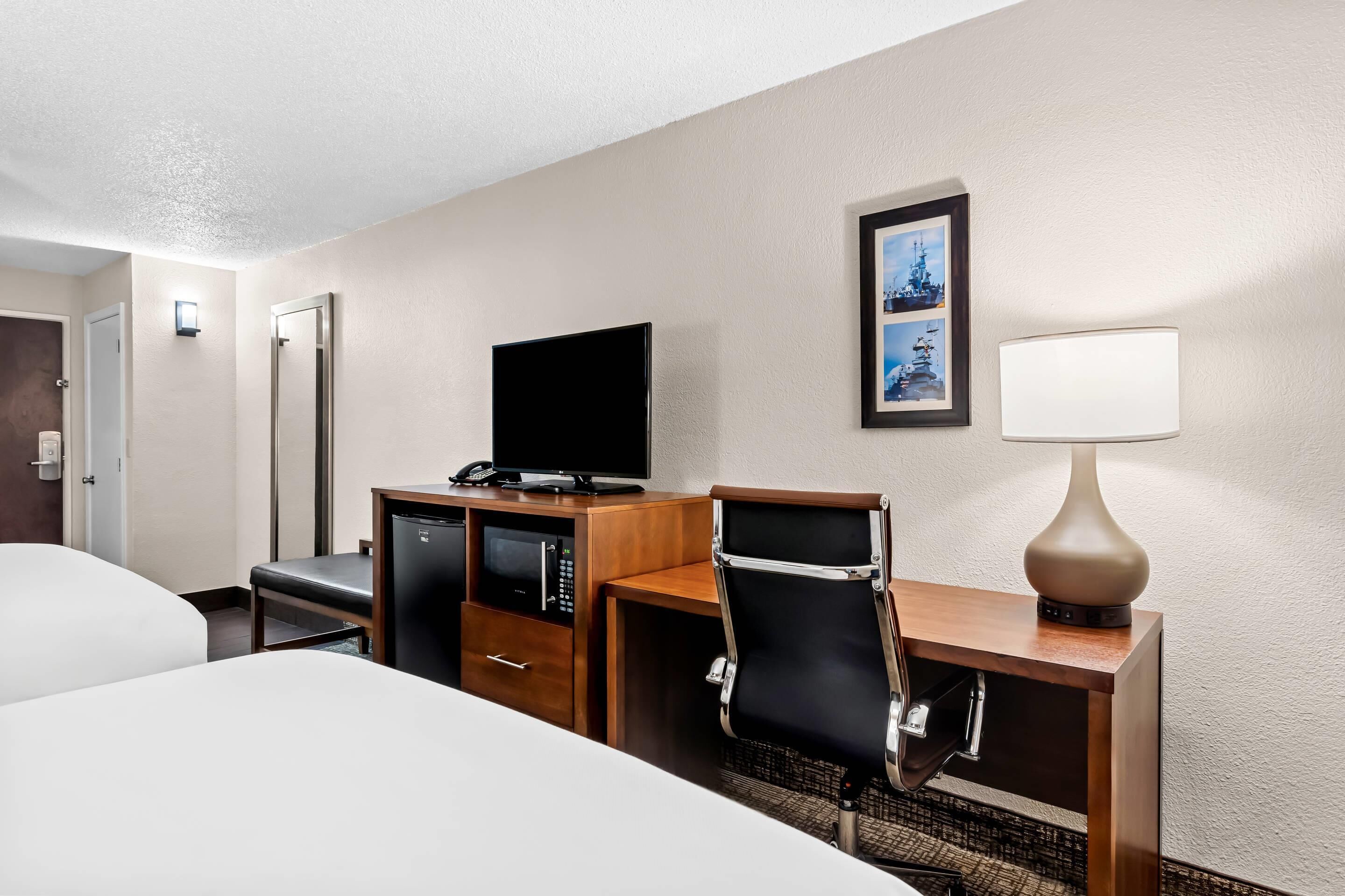 A hotel room with a bed, a desk with a computer, a television, and a lamp.