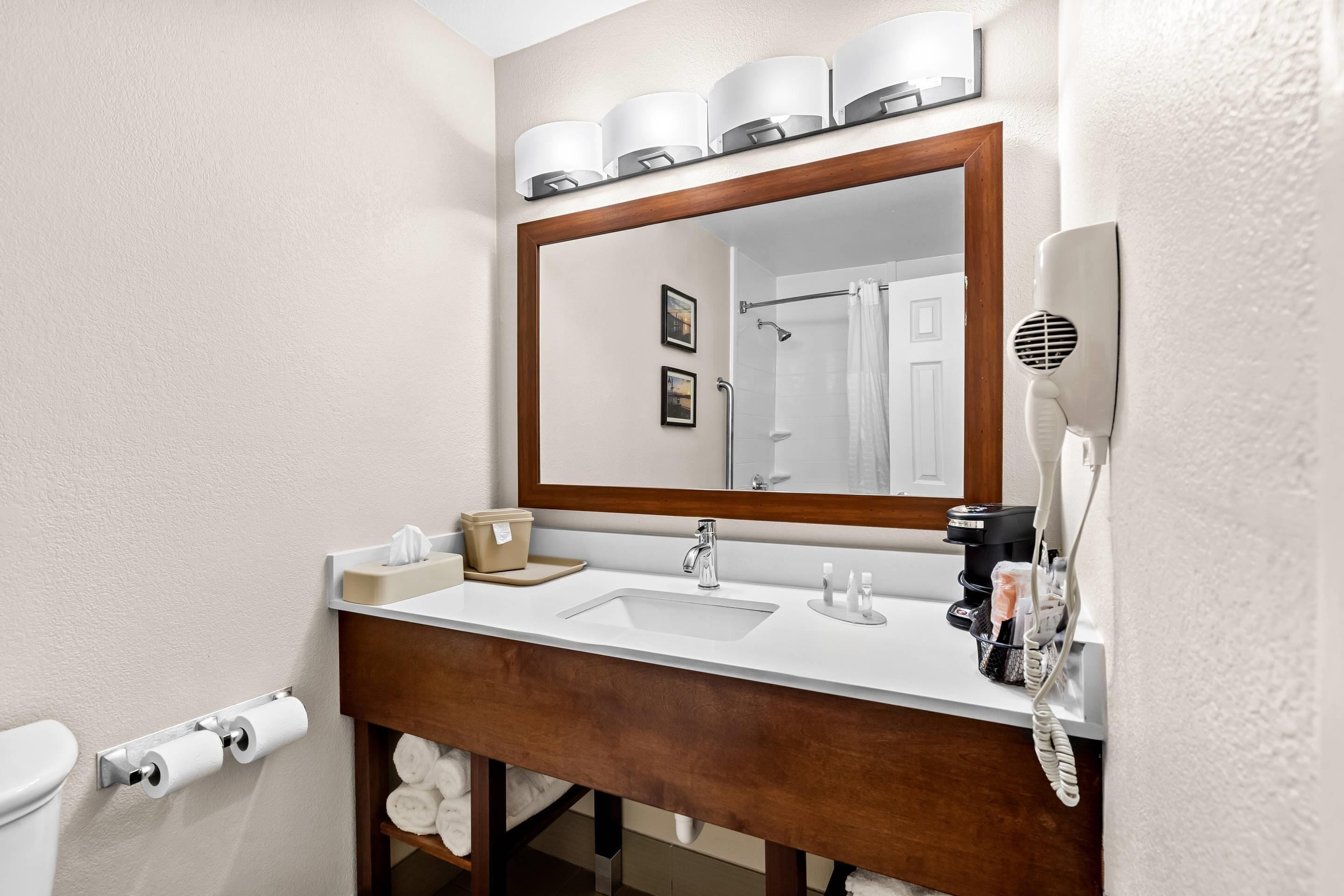 Un baño con tocador de madera, un espejo grande, un secador de pelo y un perchero para toallas.